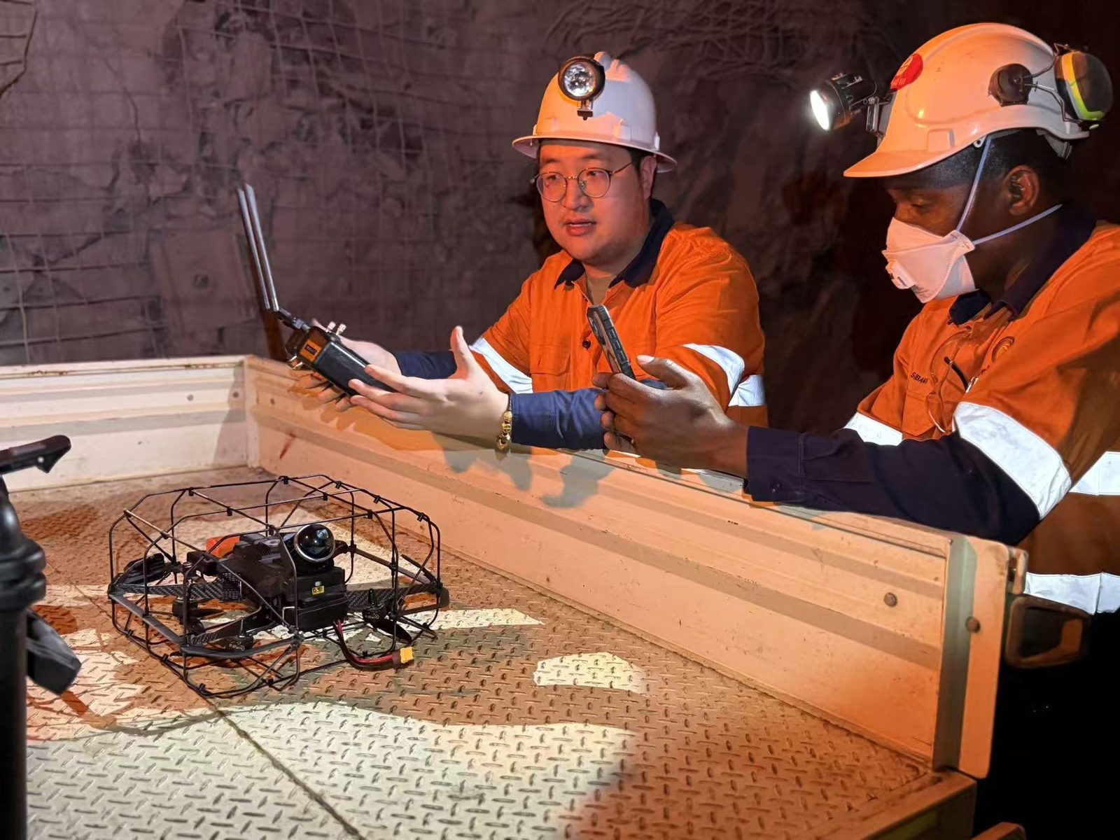 Two crew in hard hats and high-visibility shirts discussing the Kookaburra drone sitting on a light vehicle tray underground